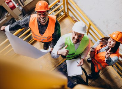 Three factory workers in safety hats discussing manufacture plan